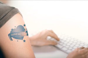 Person with an arm tatoo typing on a keyboard