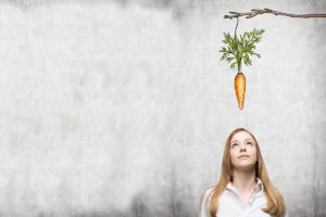Woman looking up at a carrot being held by a stick