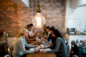 A group of professionals sitting at a long table with a lightbulb in the foreground